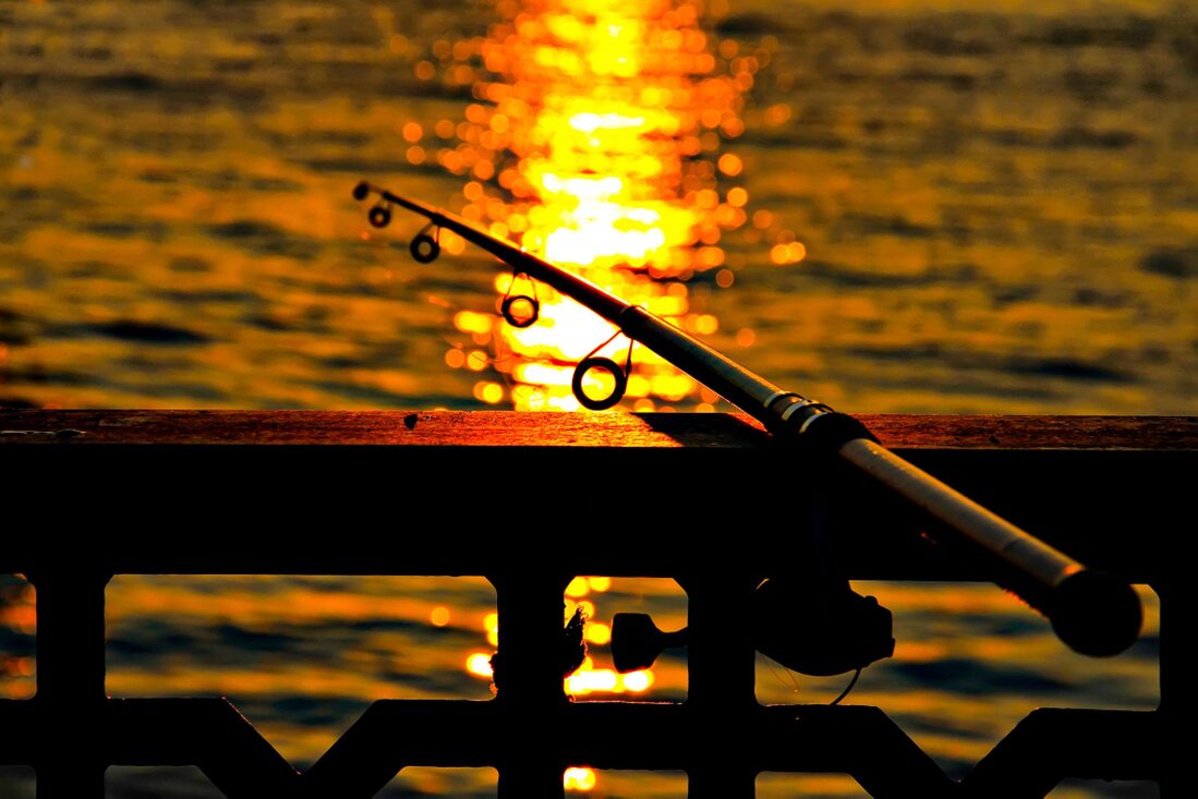 Person fishing from the back of a small boat in calm water